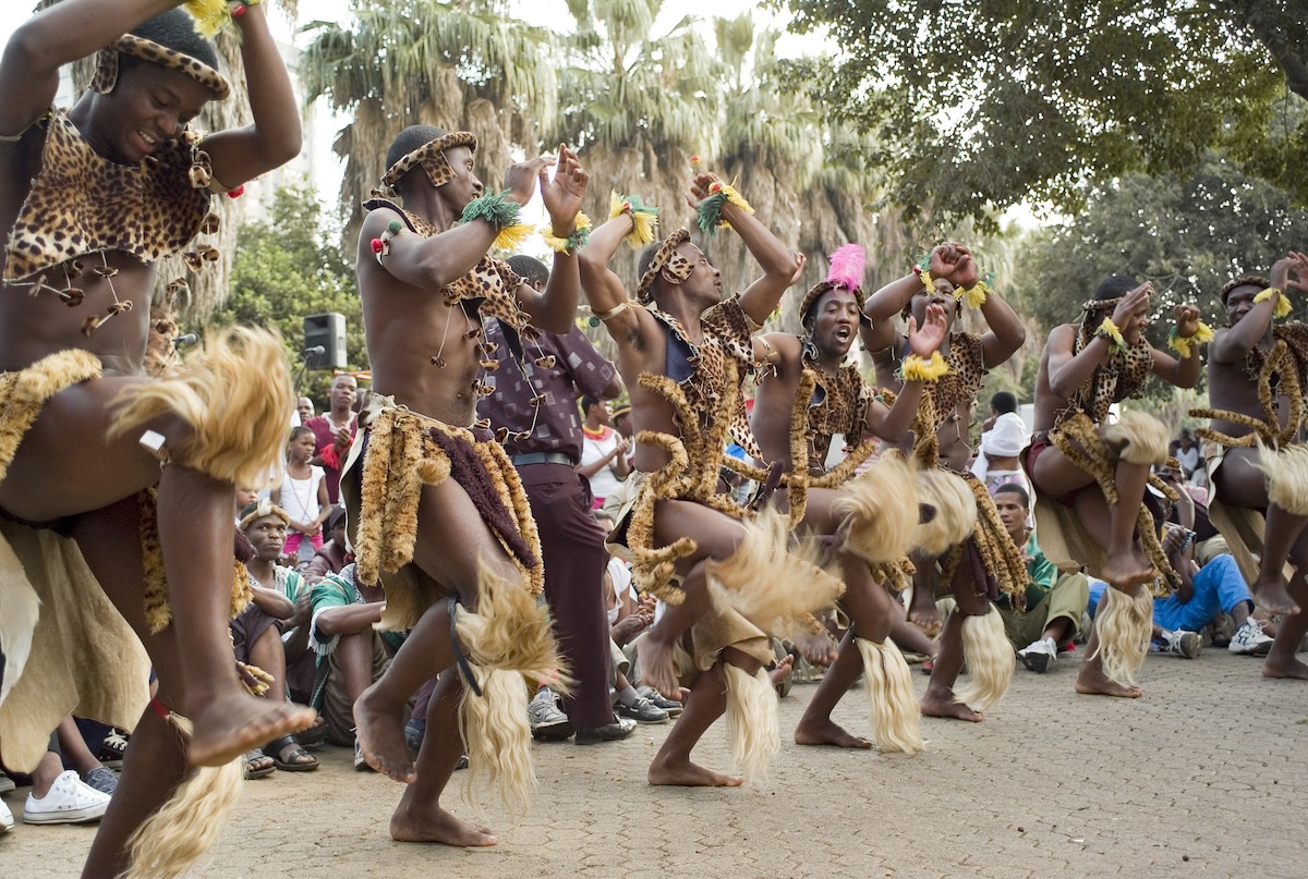 A group of Zulu dancers performing a traditional dance in vibrant attire during a cultural festival in Joubert Park, Johannesburg.