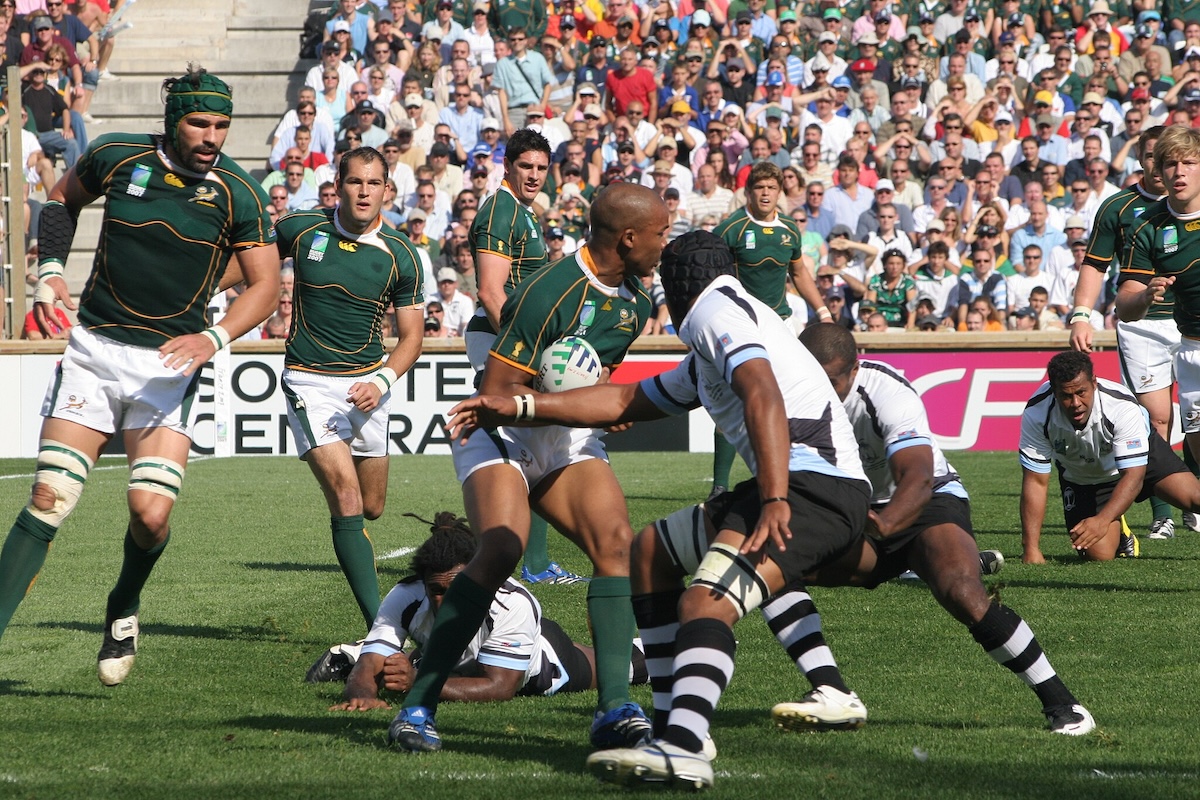 An action-packed rugby match with players in the green and gold South African jerseys, surrounded by a full stadium of spectators.