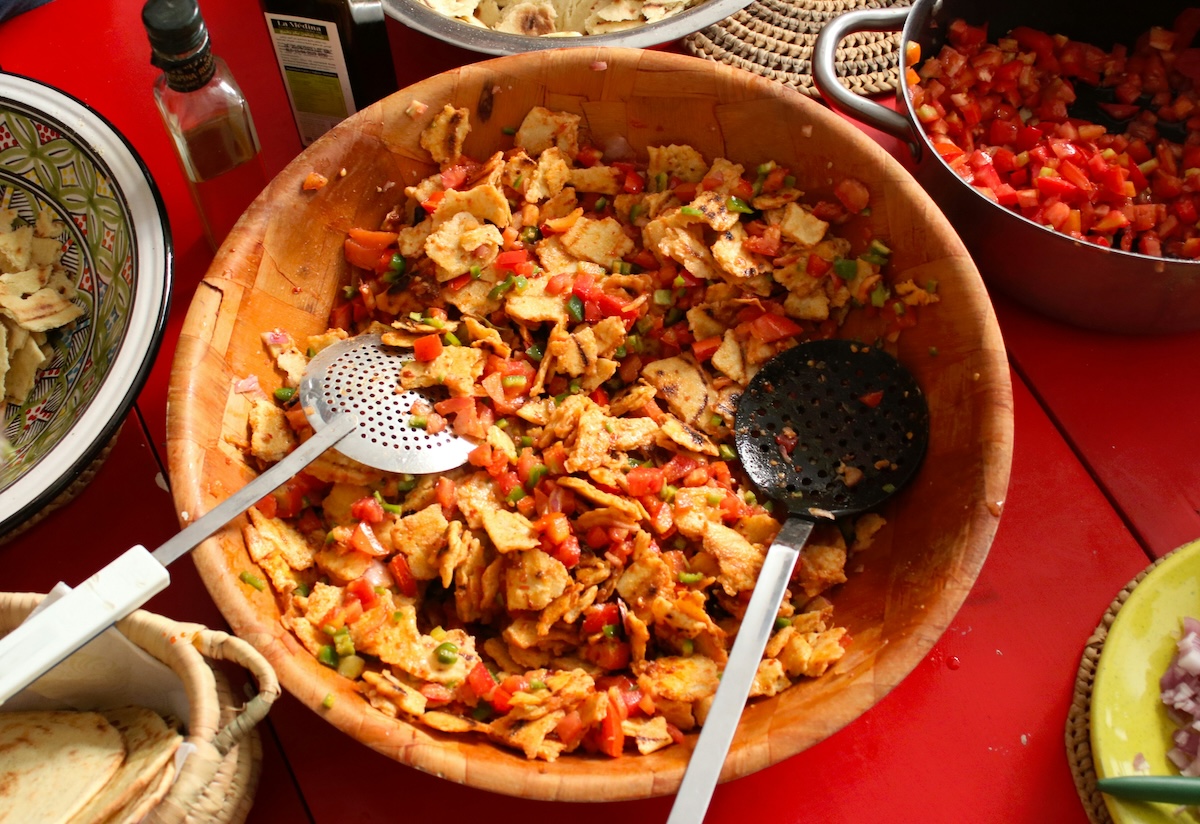 A close-up of a traditional Tunisian dish in a wooden bowl, featuring a colorful mix of vegetables and bread.