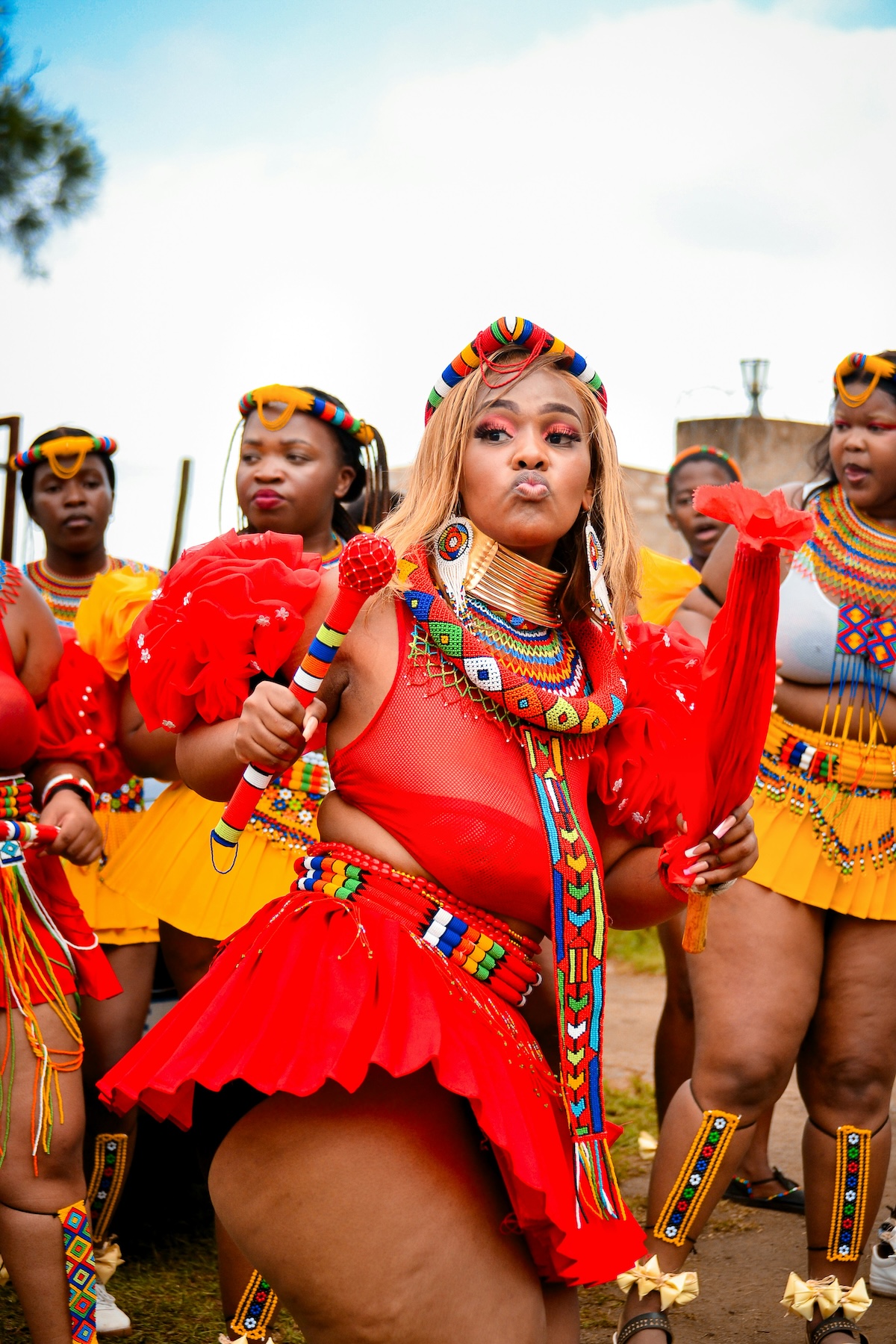 A group of Zulu women in traditional attire, performing a dance, with vibrant red, yellow, and beaded decorations.