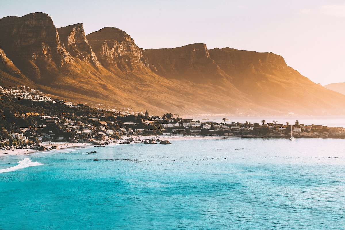 A stunning coastal view of Cape Town with clear blue waters and the majestic Table Mountain in the background at sunset.