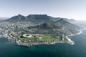An aerial view of Cape Town, highlighting the iconic Table Mountain, Lion's Head, and the cityscape along the coastline.